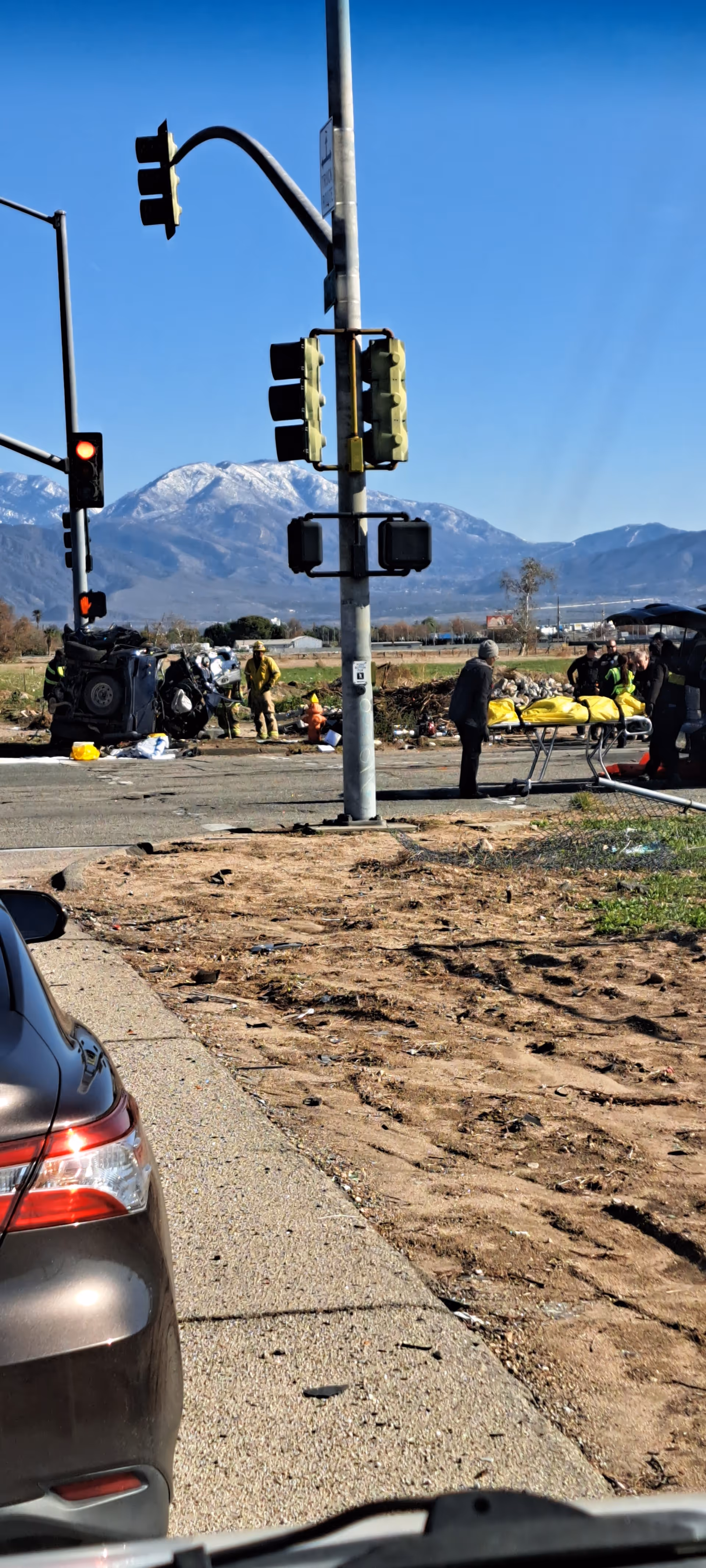 Outdoor accident scene with a crashed car, responders, and onlookers near traffic signals.