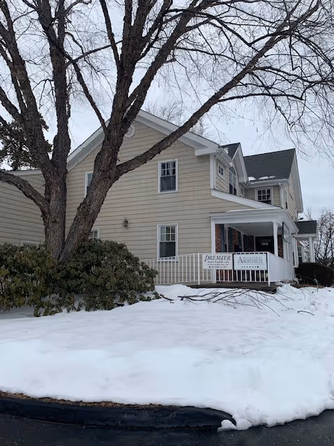 Two-story beige senior living facility with a snow-covered yard and front porch.