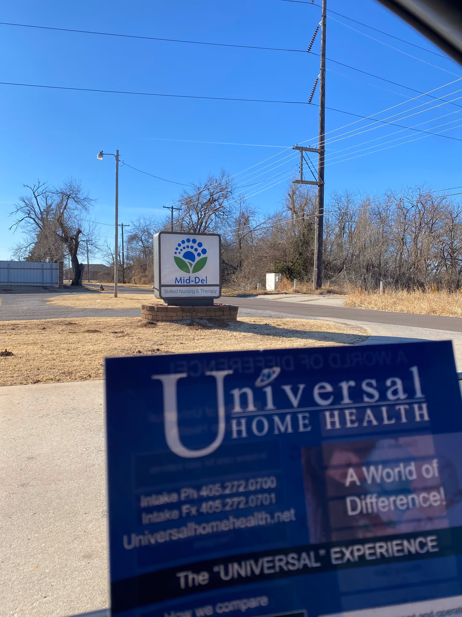 Outdoor facility entrance with a round Mid-Del sign and a Universal Home Health flyer.
