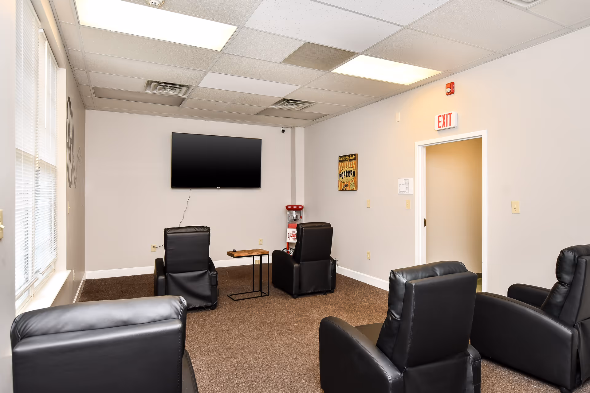 A quiet senior living lounge with black leather recliners, wall TV, and exit door.