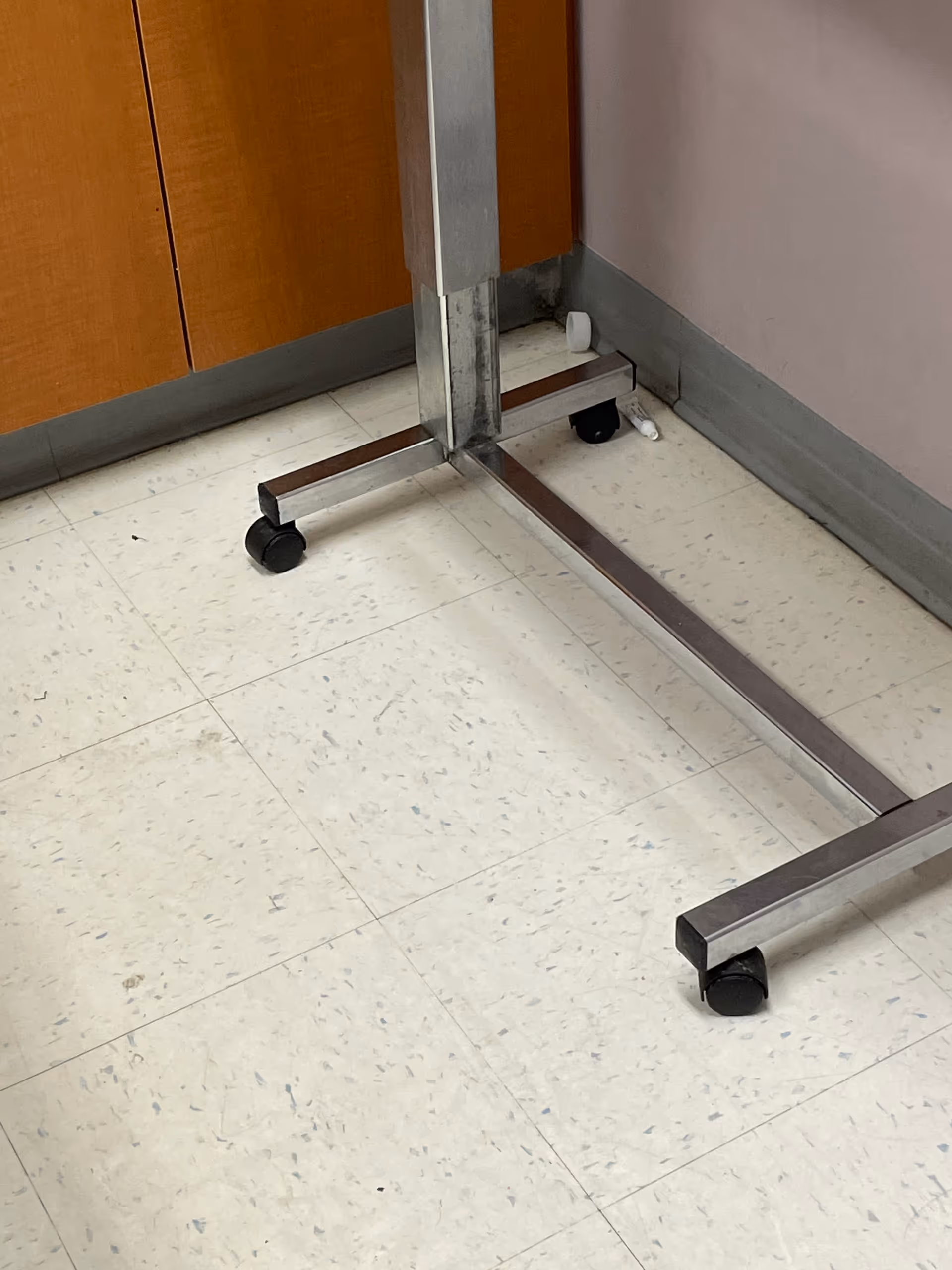 A metal hospital bed frame on wheels stands in a corner of a clinical room.