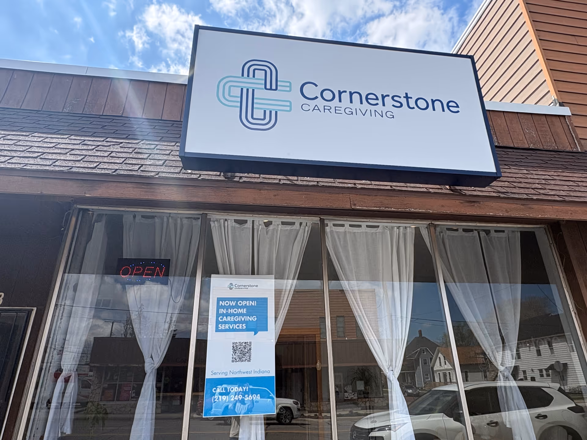 Storefront for Cornerstone Caregiving with open sign, white curtains, and posters.