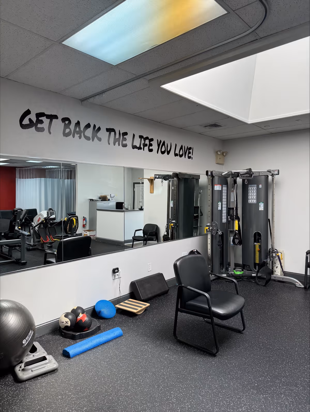 Interior workout room with gym machines, weights, mirror, and motivational slogan on wall.