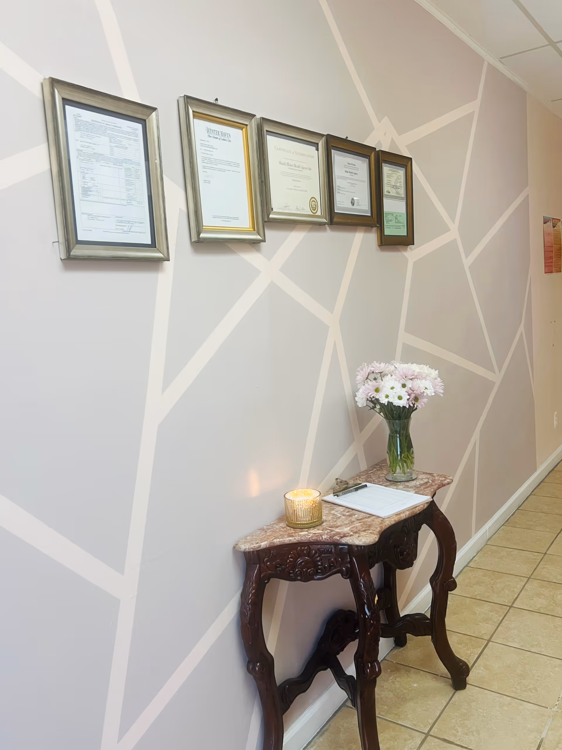 Decorative hallway wall with framed certificates above a marble console table and flowers.