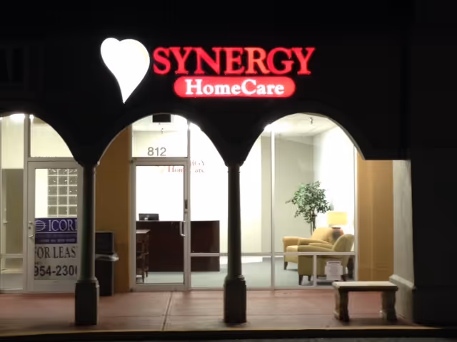 Night view of Synergy HomeCare storefront with illuminated sign and interior seating.