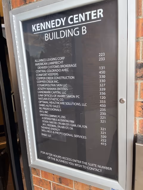 Exterior signboard listing tenants outside Kennedy Center Building B on brick wall.