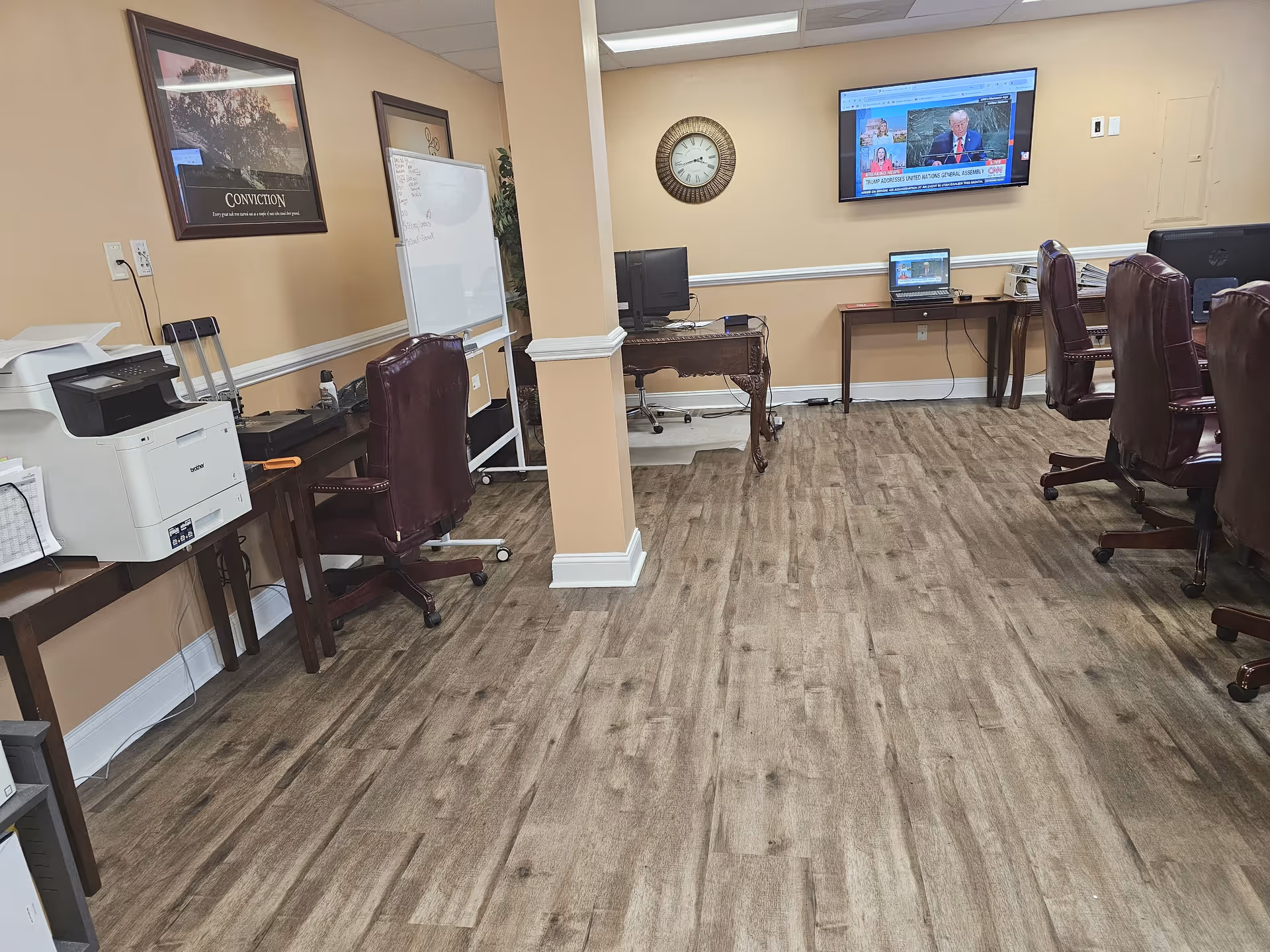 Interior administrative area with desks, chairs, a whiteboard, a wall clock, and a mounted TV.