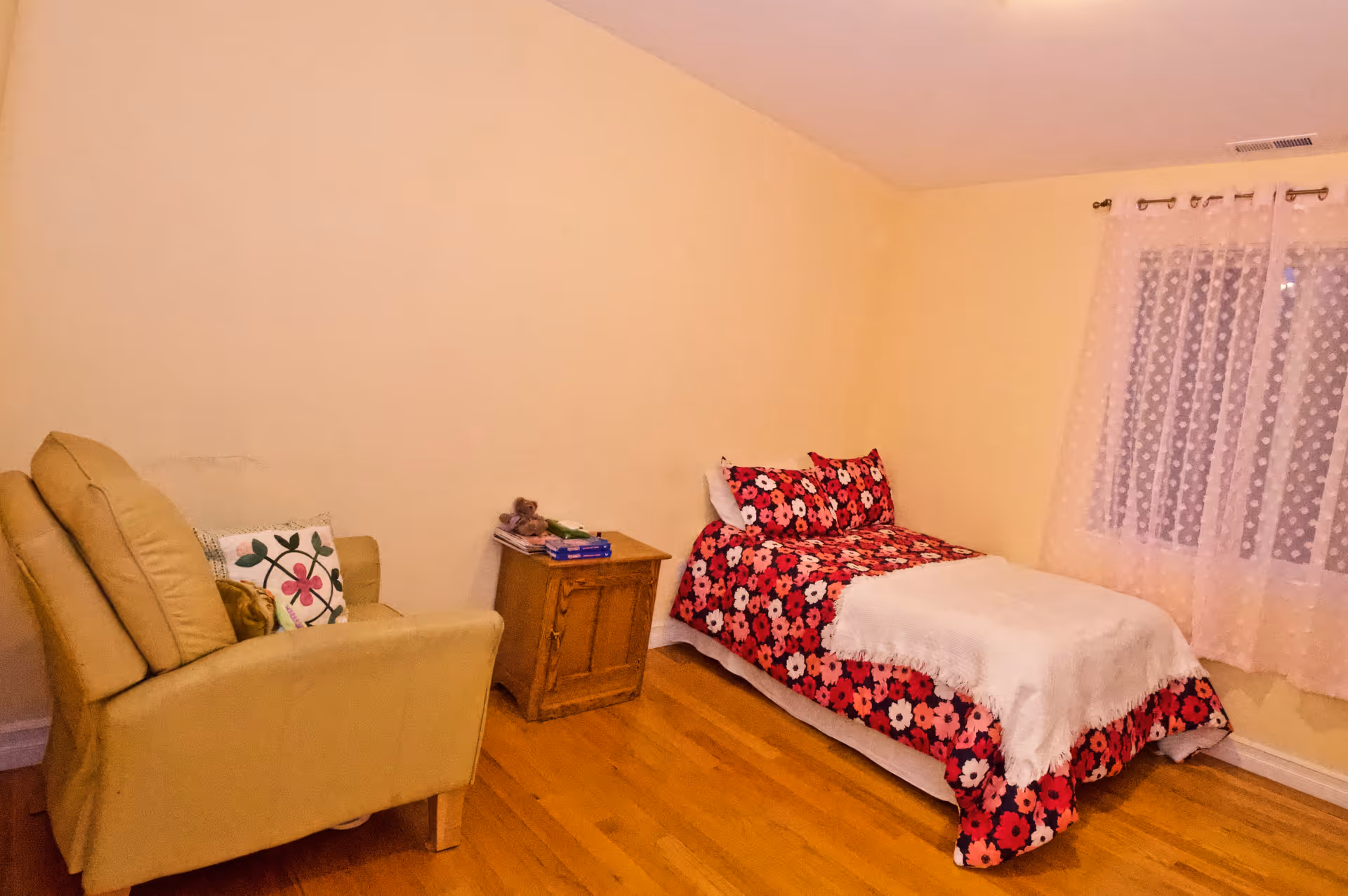 A small bedroom with a single bed, floral bedding, a chair, and a nightstand.