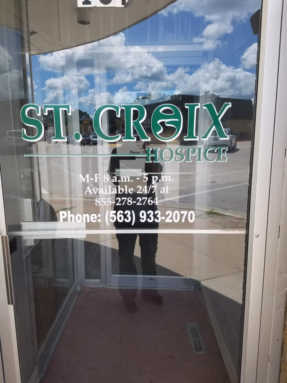 Glass entrance door reads St. Croix Hospice; reflection of person taking photo.