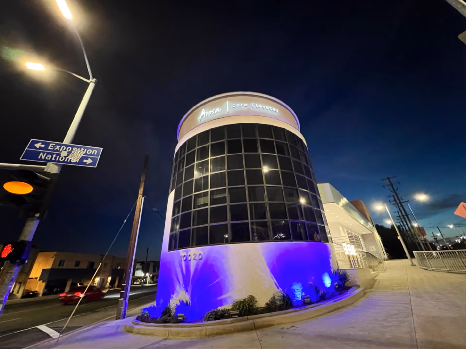 Night exterior view of an Arosa Los Angeles building with curved glass front and blue lighting.