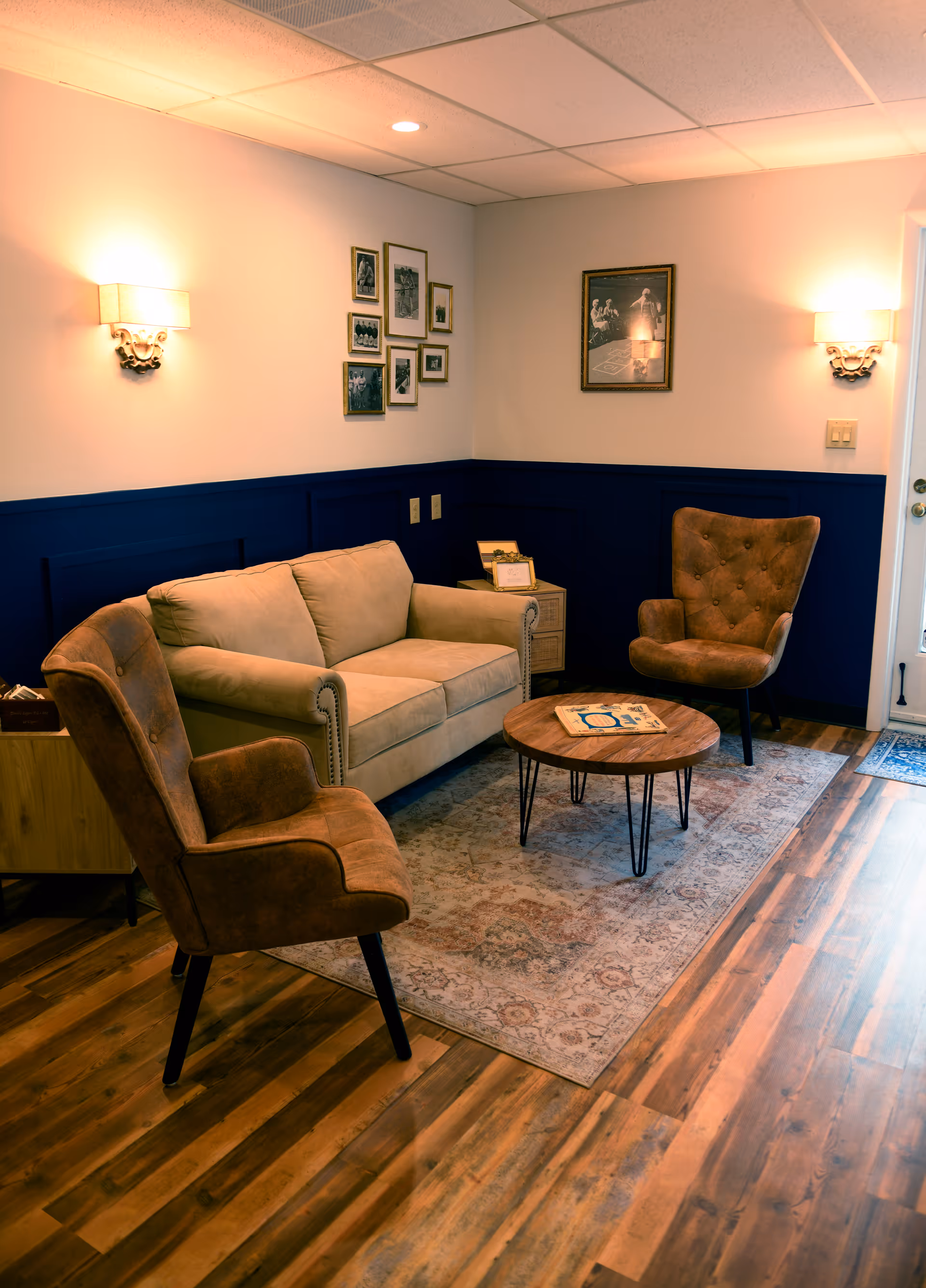 Cozy lounge area with beige sofa, brown chairs, coffee table, rug, and blue wainscoting.