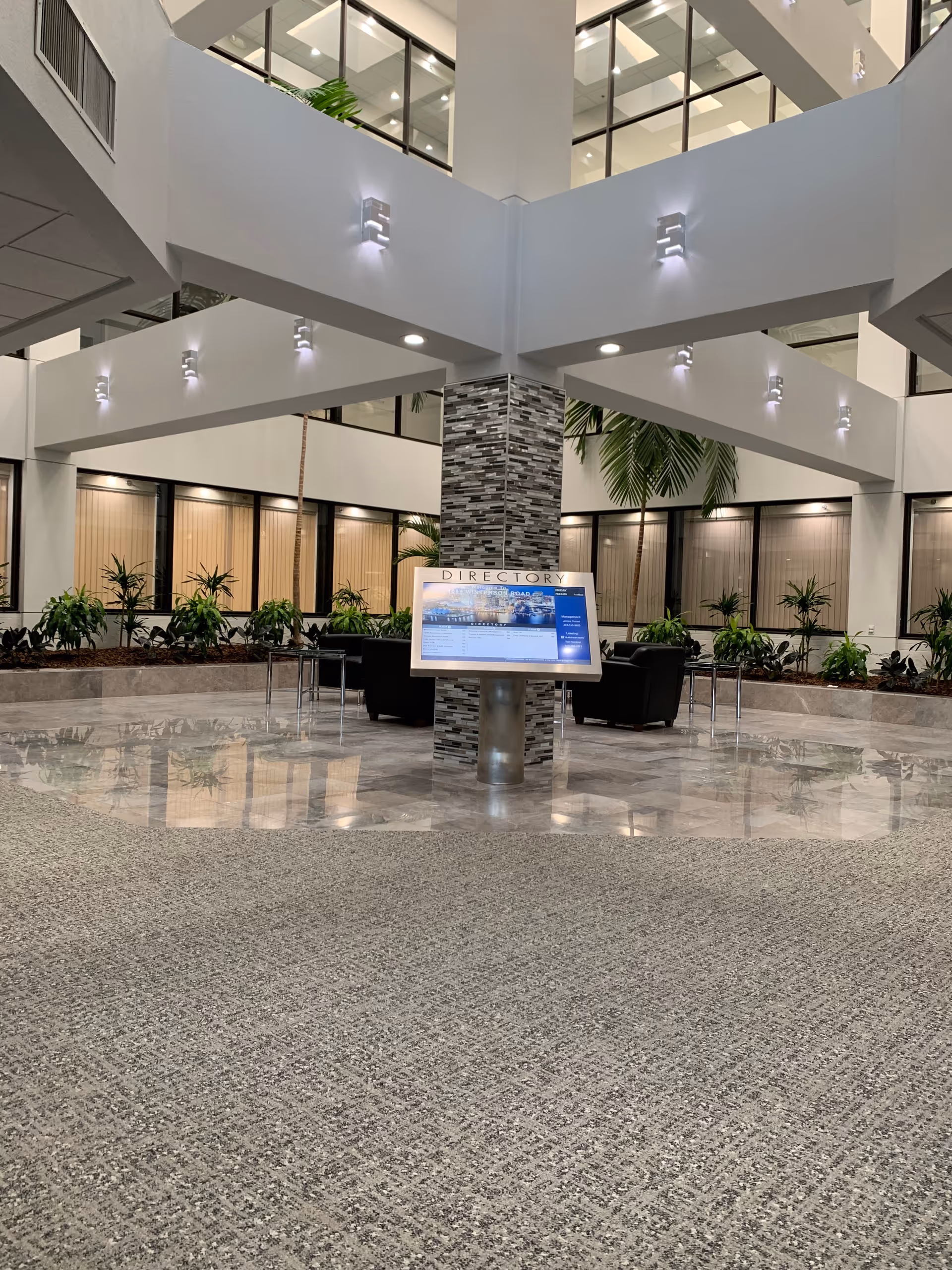 Modern indoor atrium lobby with a central directory sign and surrounding plants.