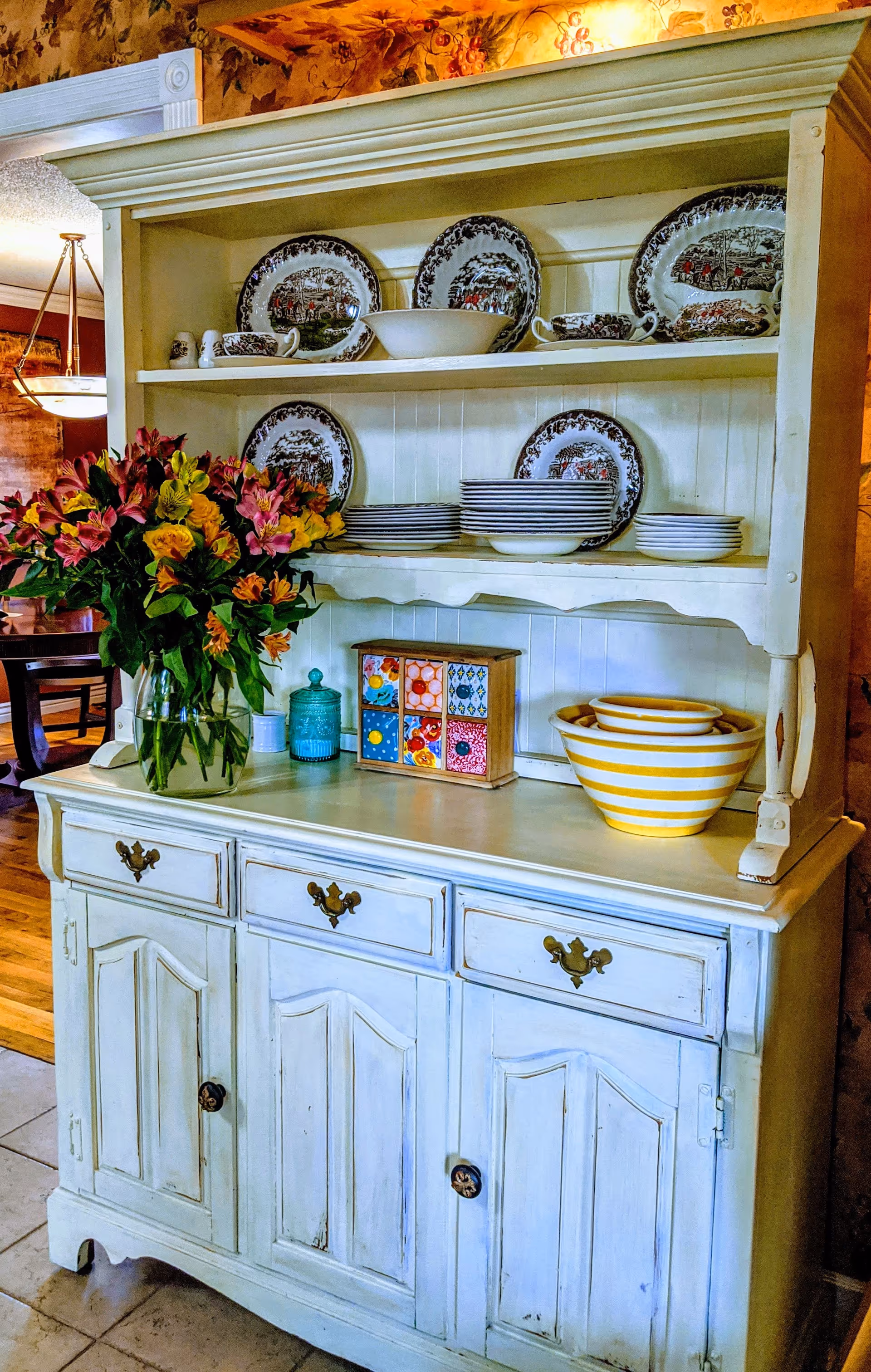 Cream-colored dining hutch displaying plates, bowls, and a bouquet on the counter