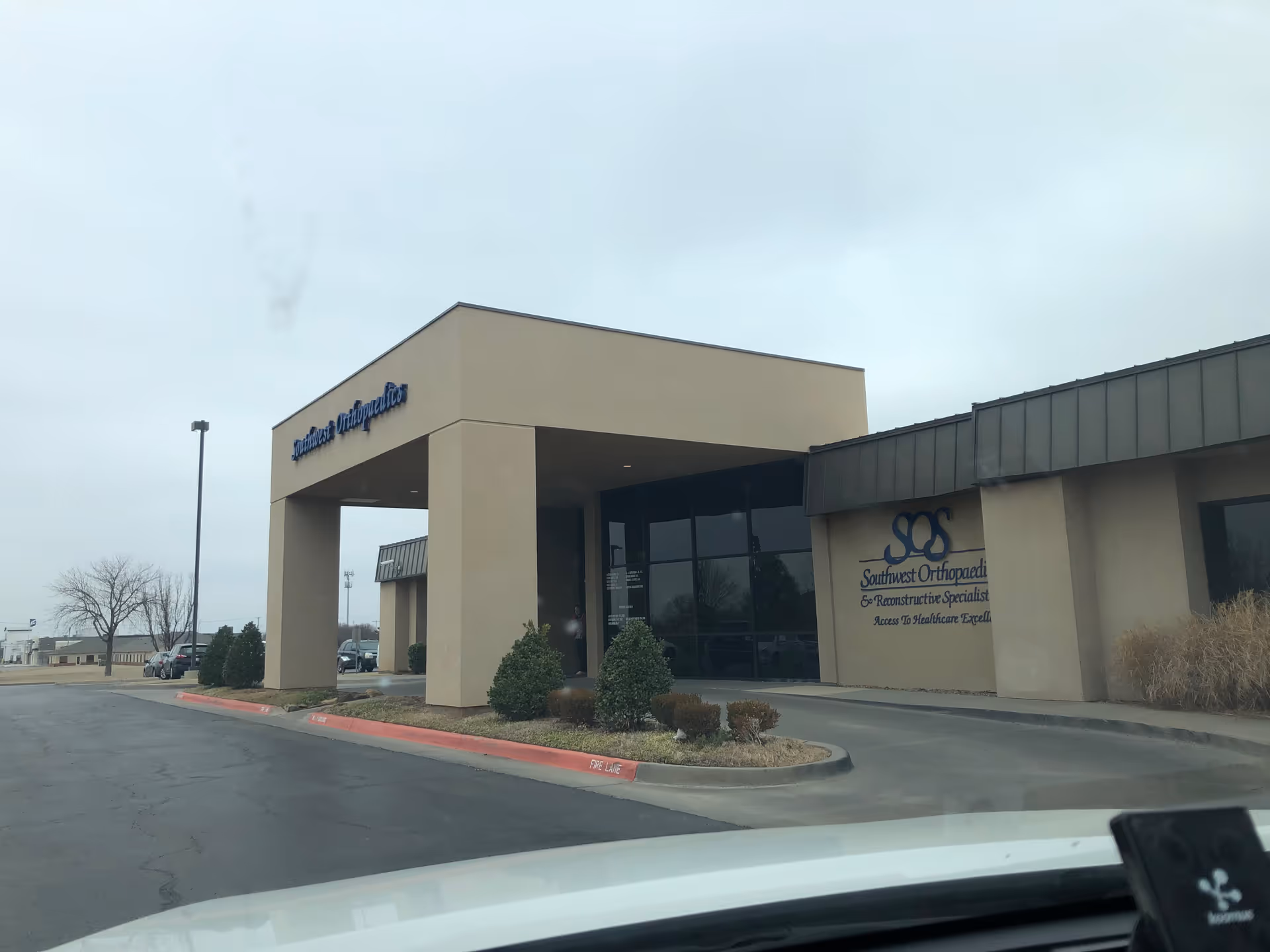 Exterior view of a beige clinic building with a covered entrance and parking lot