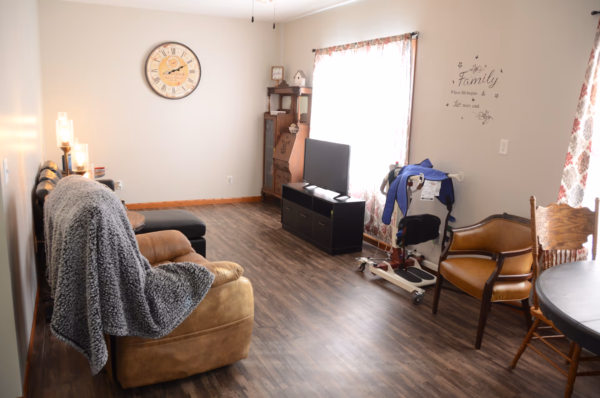 Cozy living room featuring sofa, chairs, TV stand, window drapes, and mobility equipment.