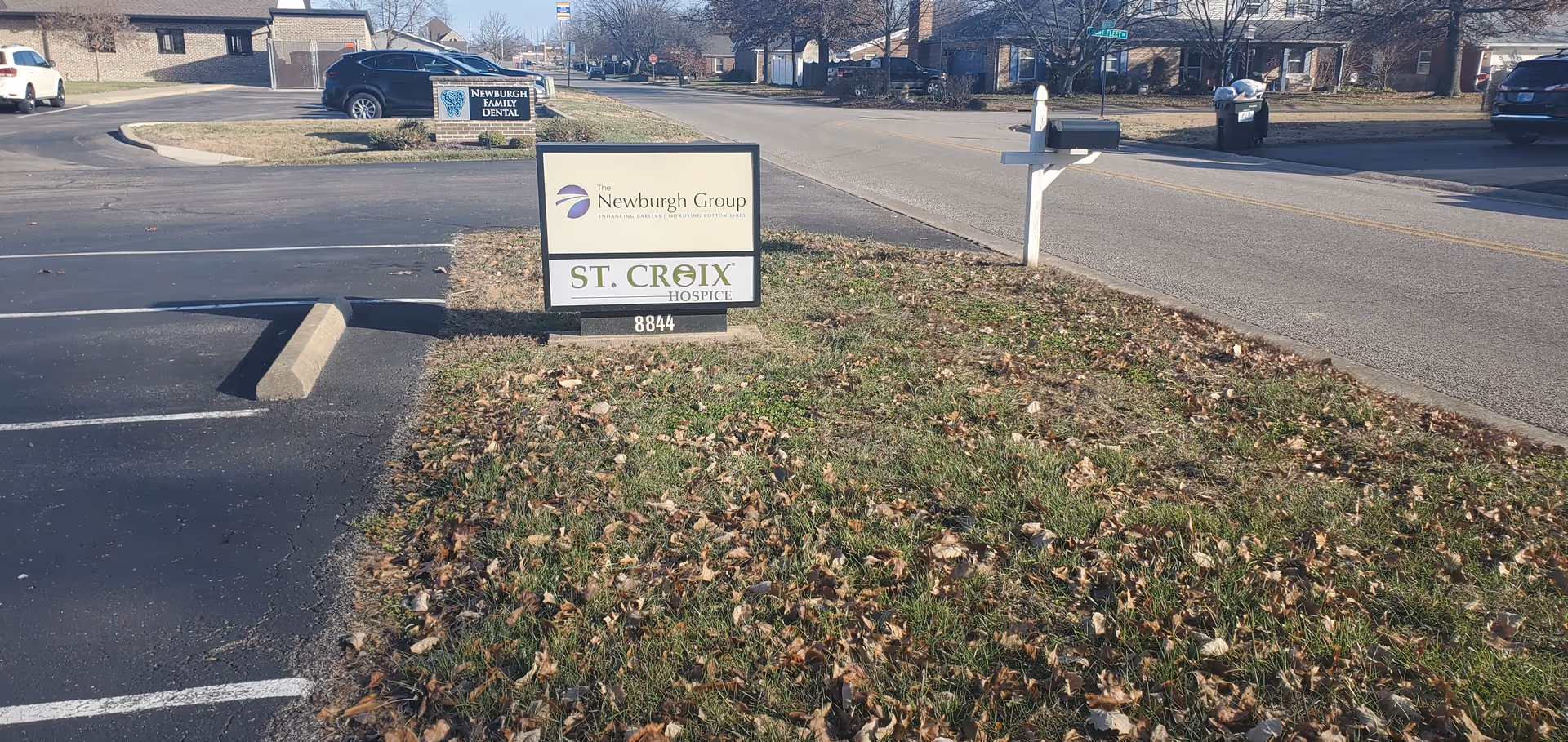 Exterior view of St. Croix Hospice sign on a grassy median by a parking lot.