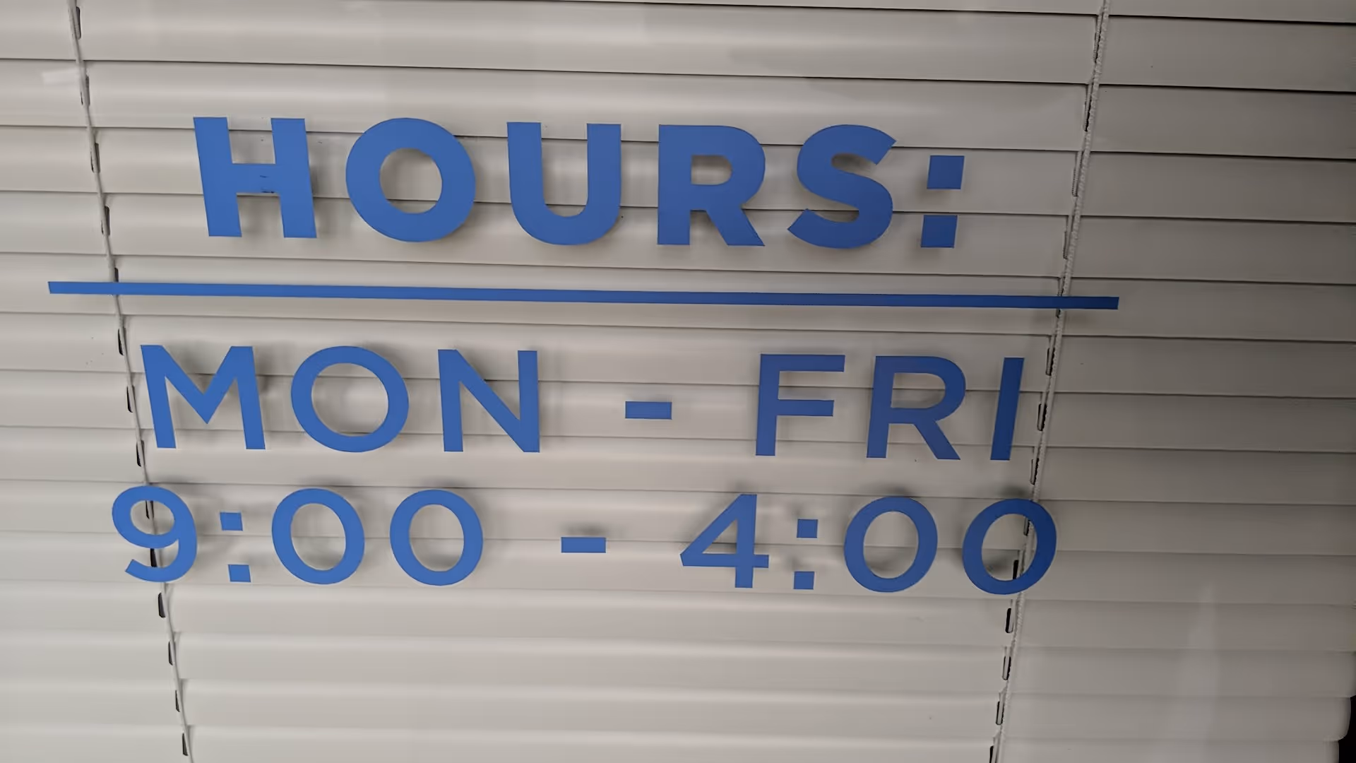 Metal shutter displaying a blue HOURS sign: Mon-Fri 9:00-4:00.