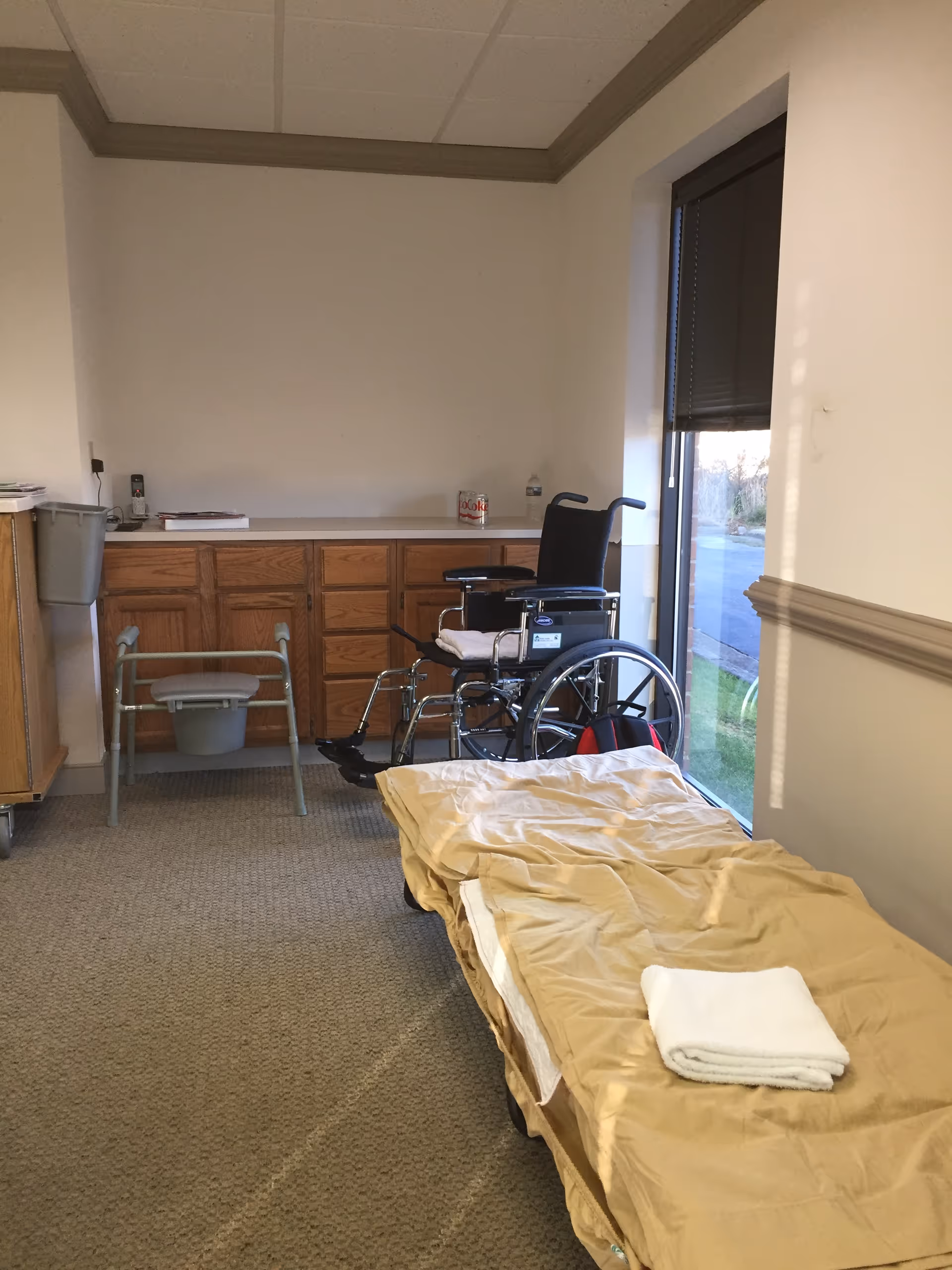 Interior room with a wheelchair, gurney, towels, and wooden cabinets along the wall.