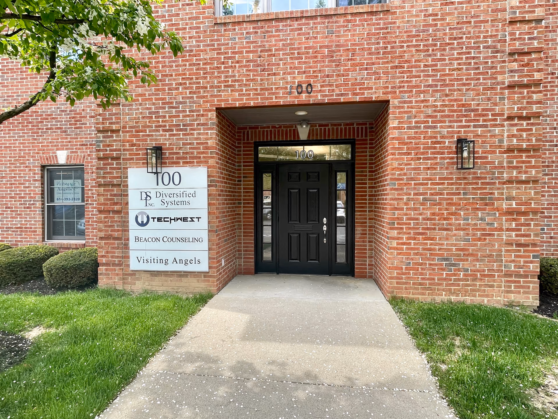 Red brick building entrance with black door and Visiting Angels signs.