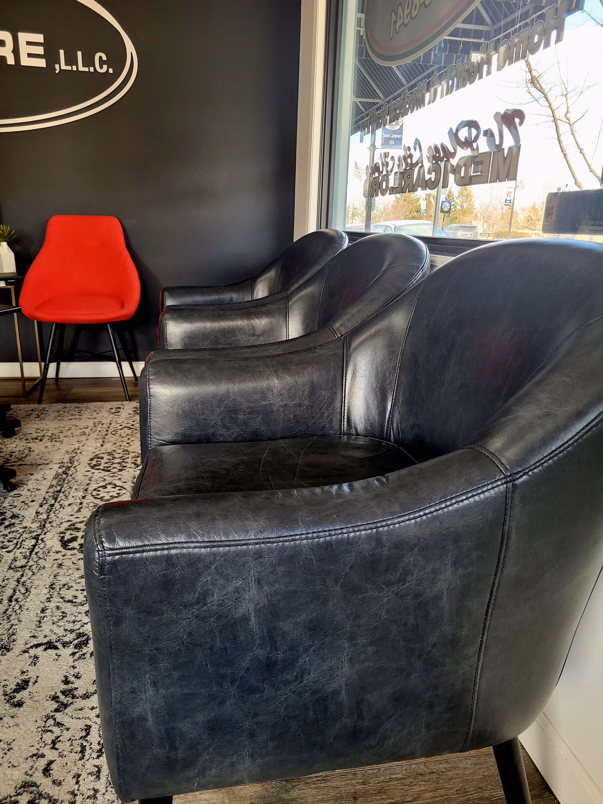 Reception lounge with black leather chairs and a red accent chair near a large window.