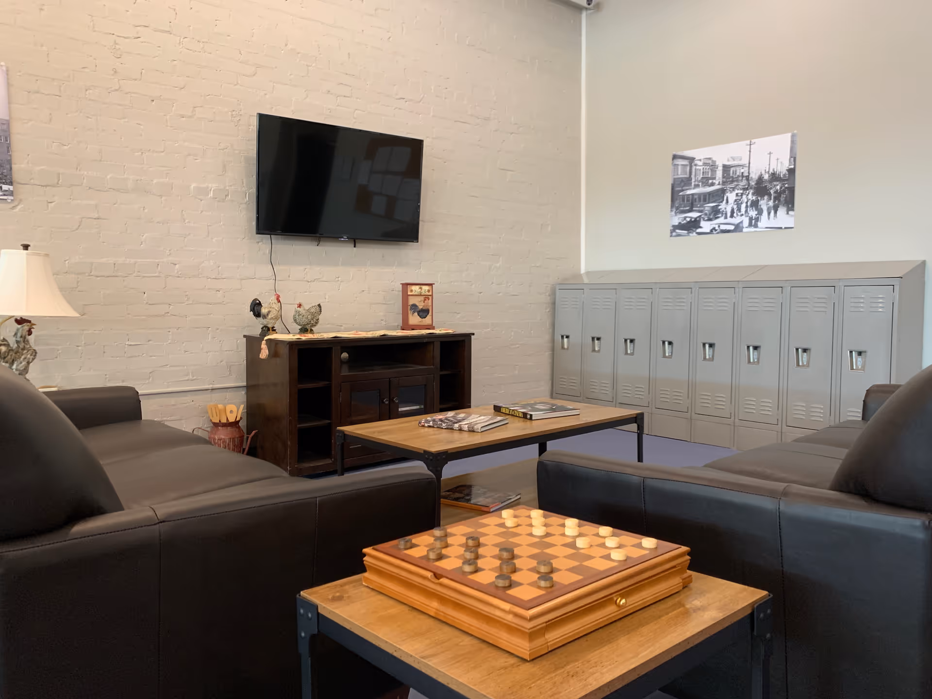 Cozy living room lounge with black leather sofas, a TV, lockers, and a chessboard table.