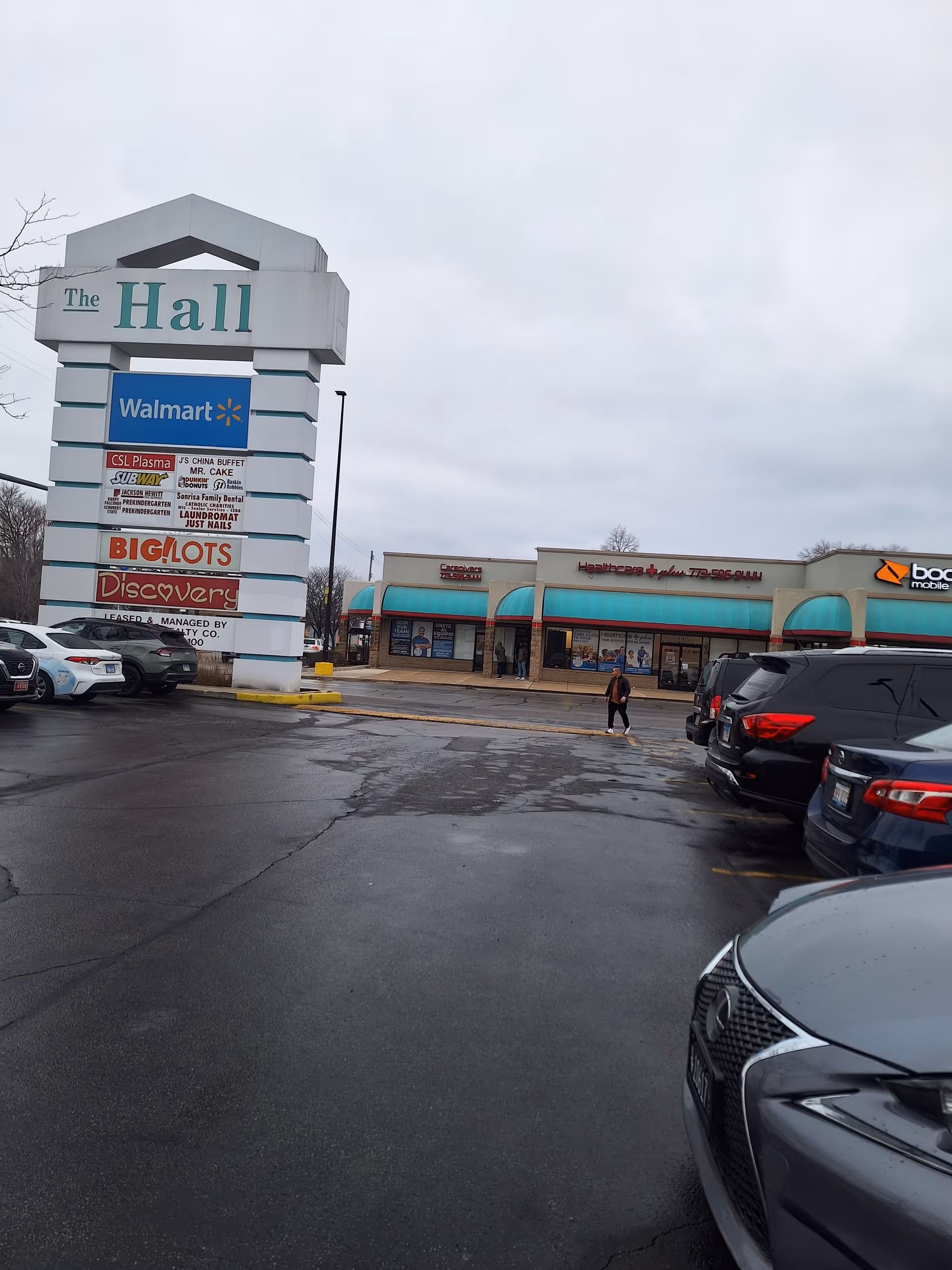 Outdoor parking lot in front of a shopping plaza with a tall sign reading The Hall.
