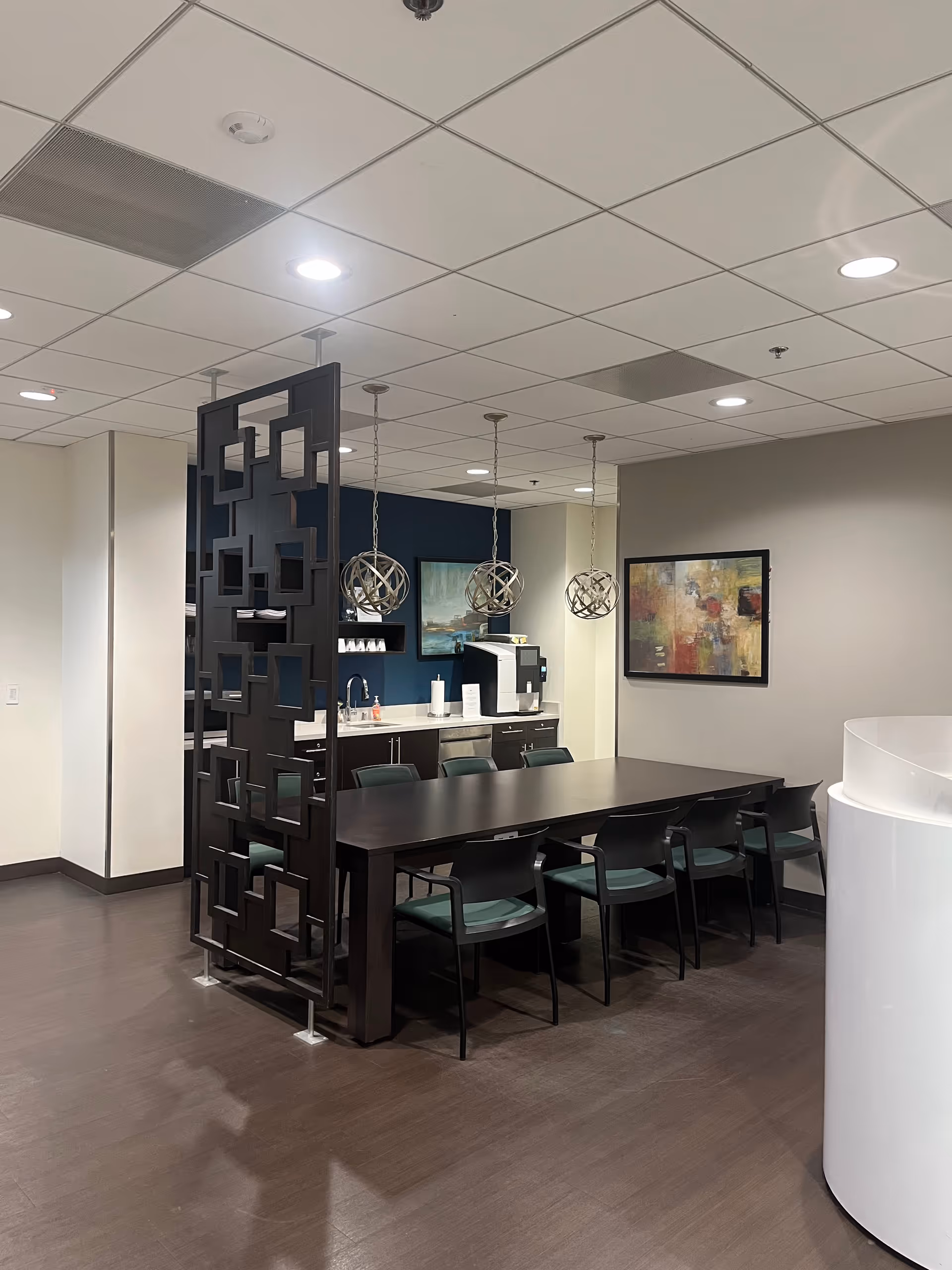 Long dark dining table with green chairs beside a kitchenette and modern pendant lighting.