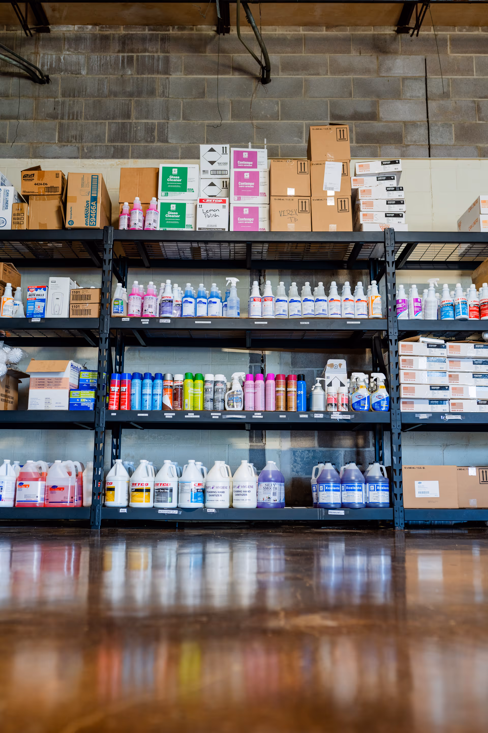 Industrial storage shelves with cleaning supplies and boxes in a facility storage room.