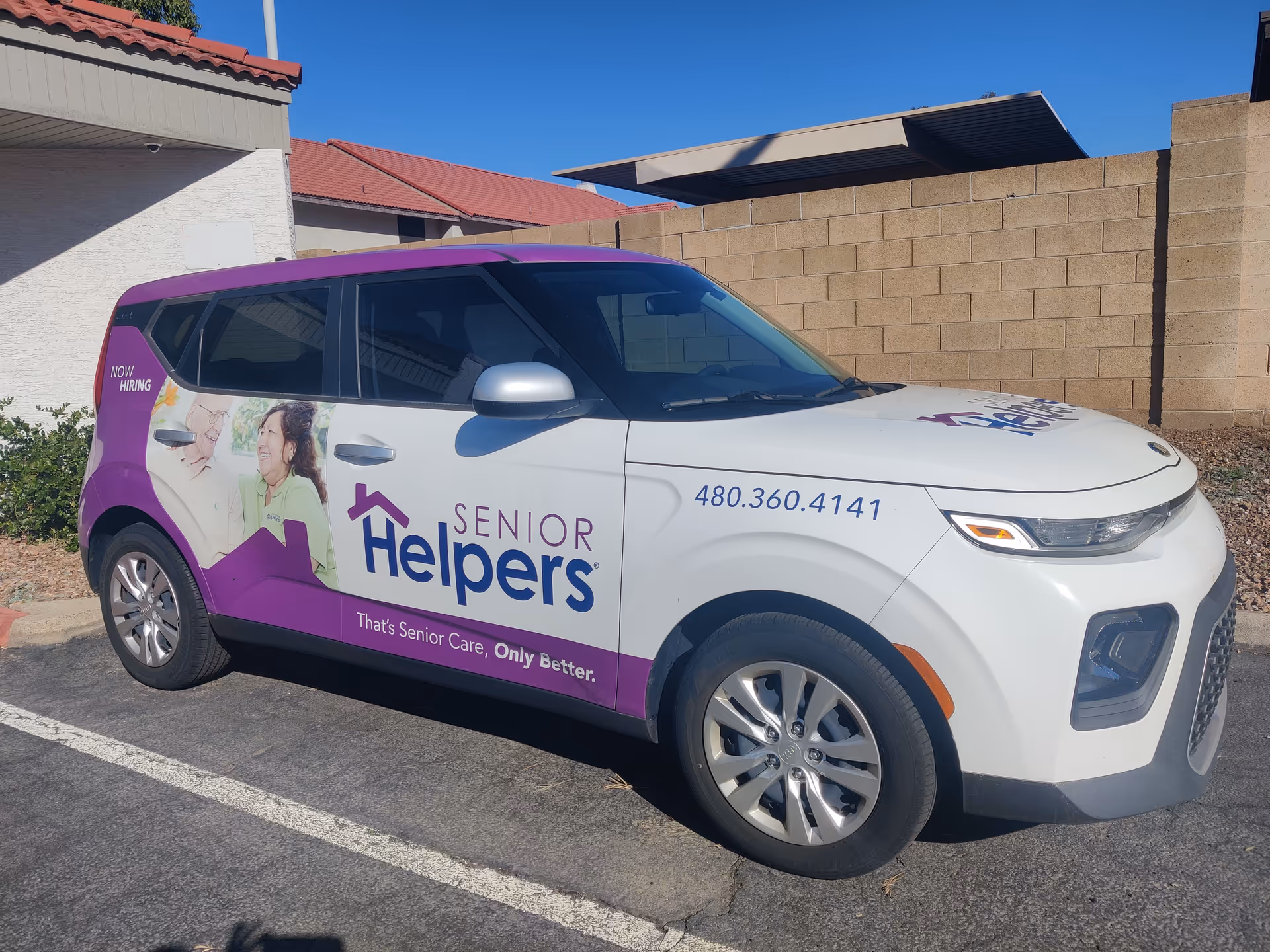 A branded Senior Helpers van parked in a lot beside a beige brick wall.