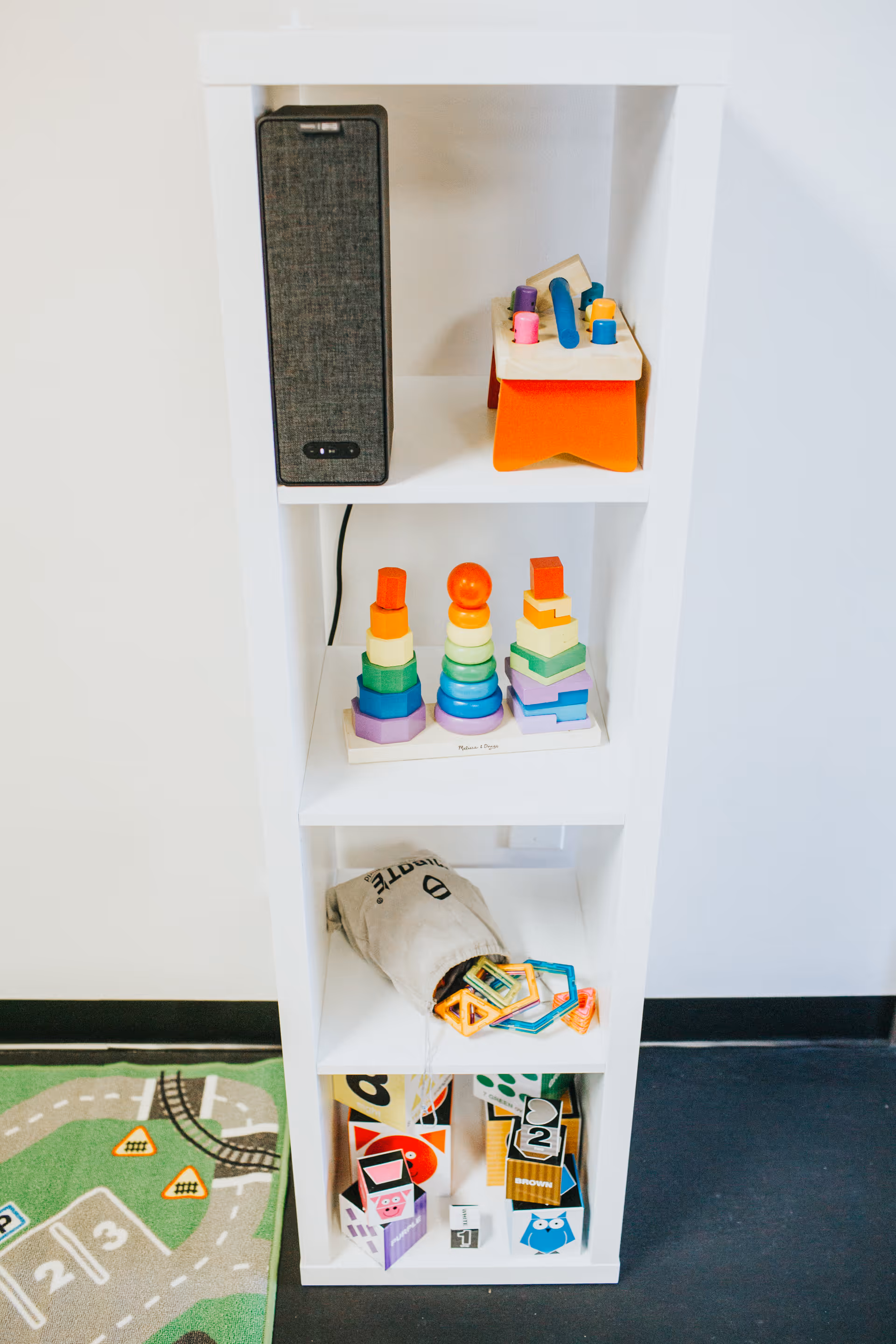 White bookshelf with colorful wooden stackable toys and a speaker.
