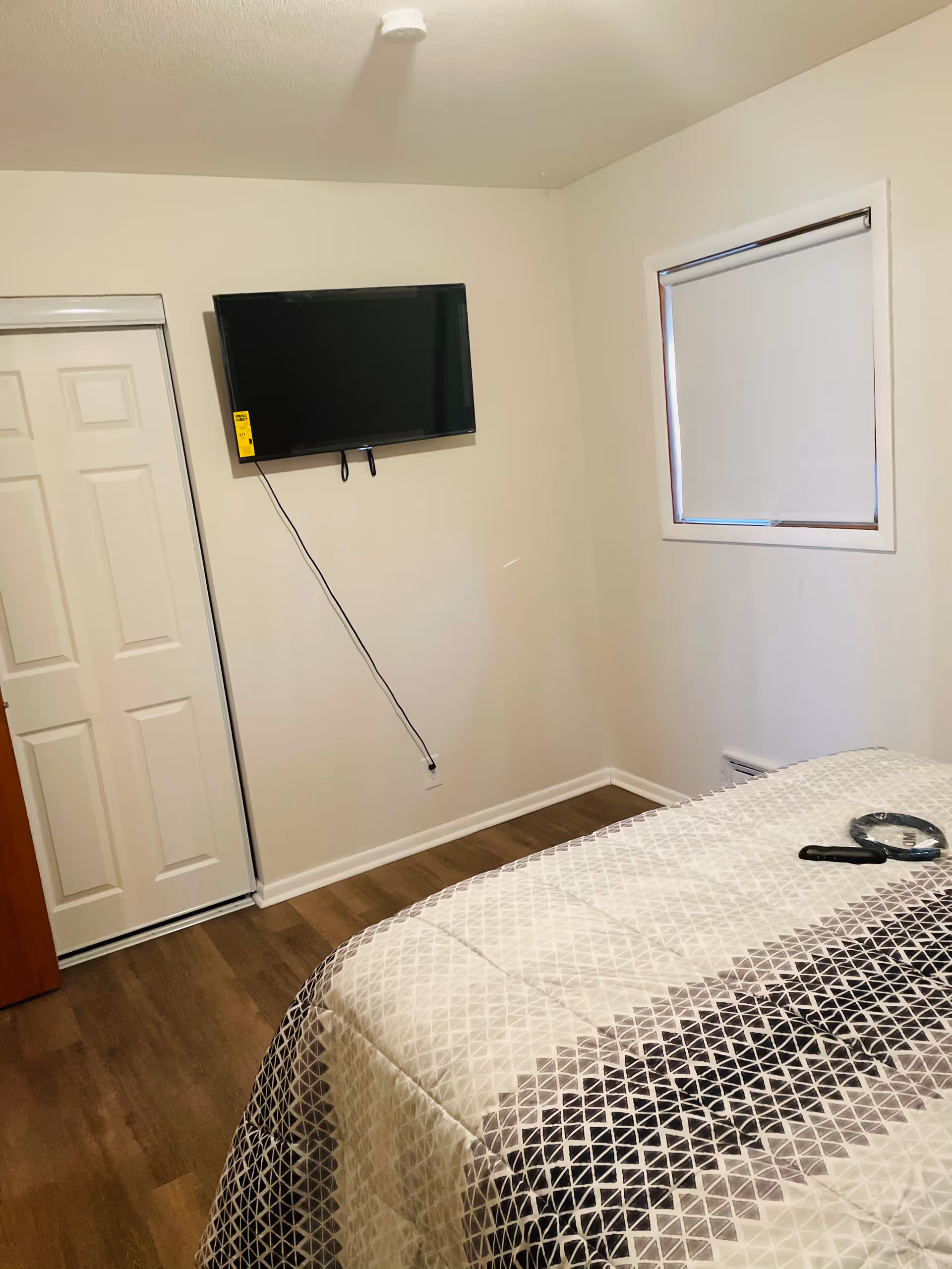 Compact bedroom with wall-mounted TV, window, closet door, and bed with a geometric quilt.