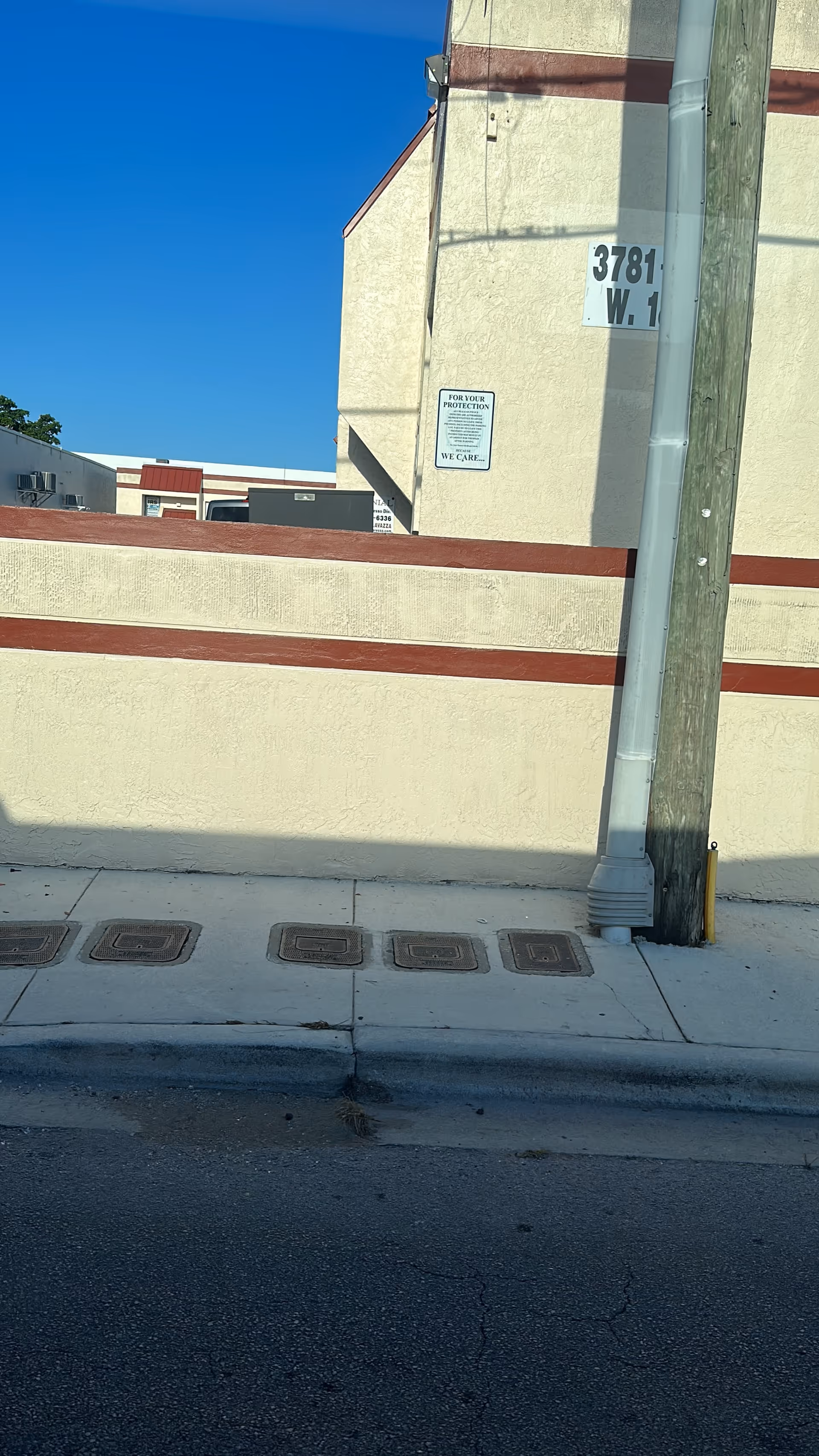 Beige building exterior with a sidewalk, utility pole, and blue sky.