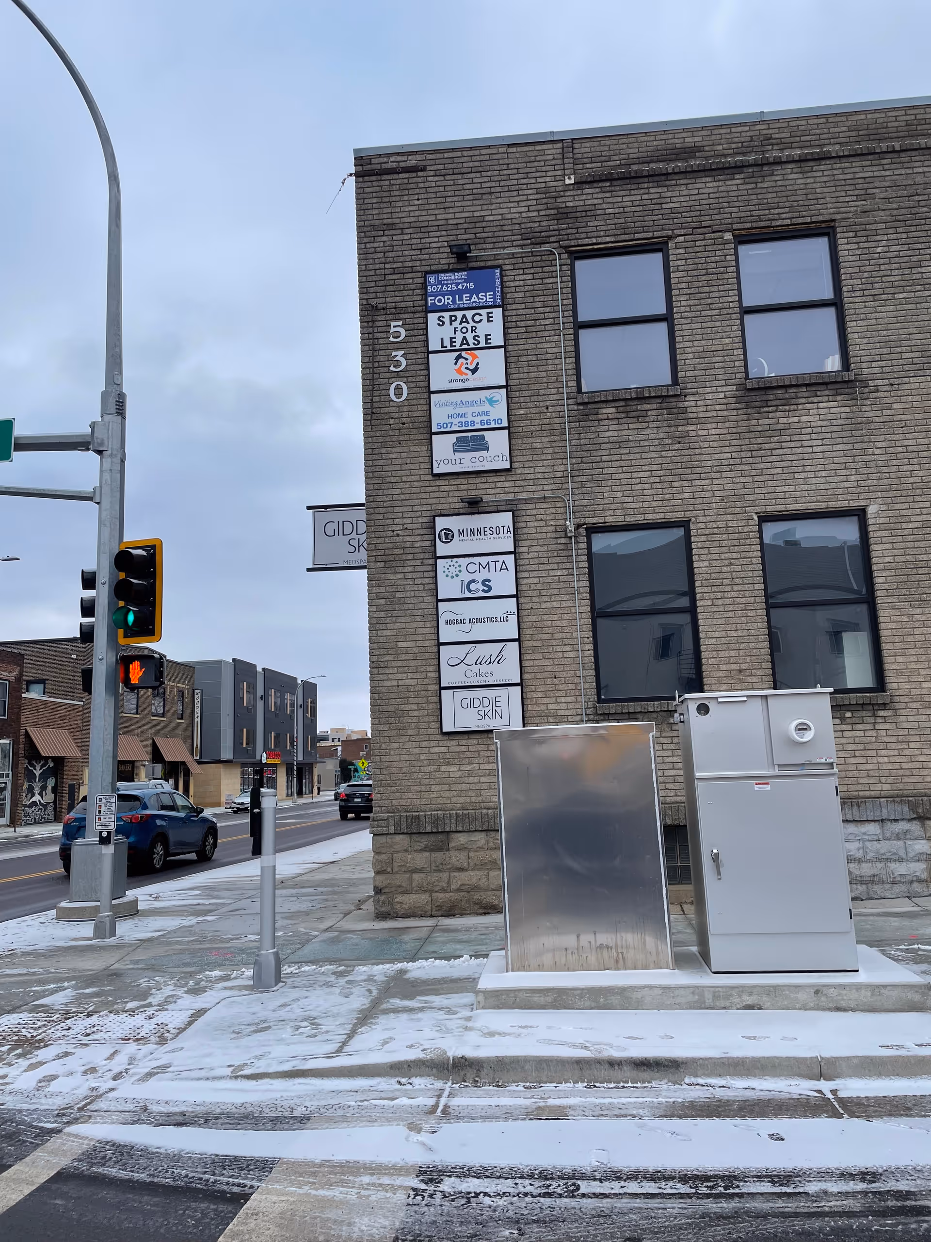 Street view of a brick building with multiple for-lease signs and utility boxes.