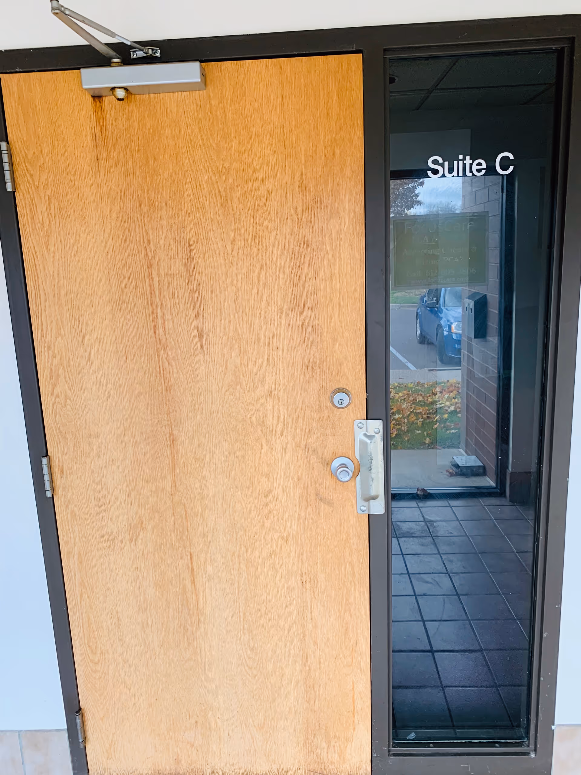 Wooden door beside glass entry labeled Suite C in a building hallway.
