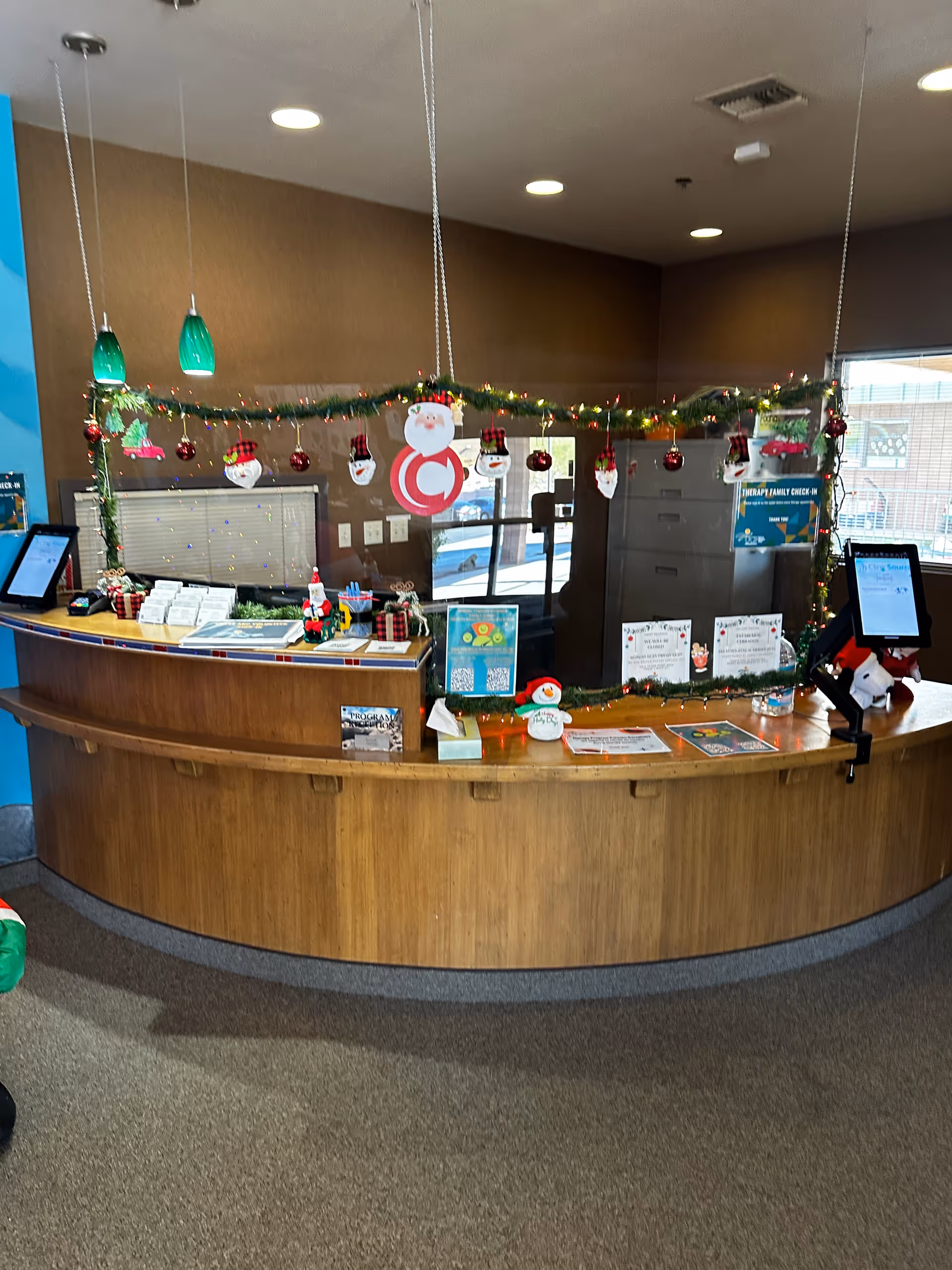 A curved wooden reception desk in a facility lobby decorated with Christmas garlands.