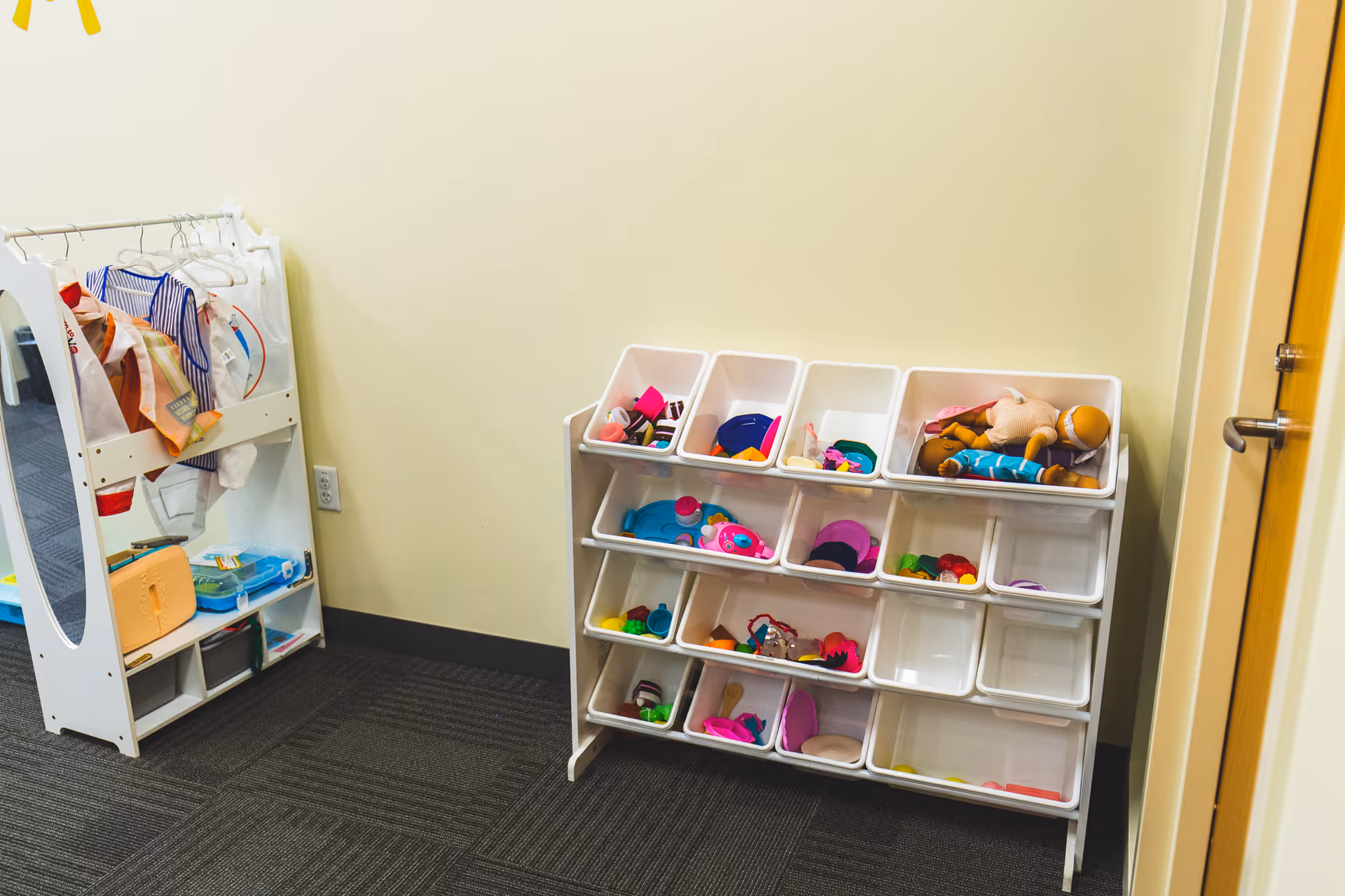 Small play area corner with white cubby storage filled with colorful toys.