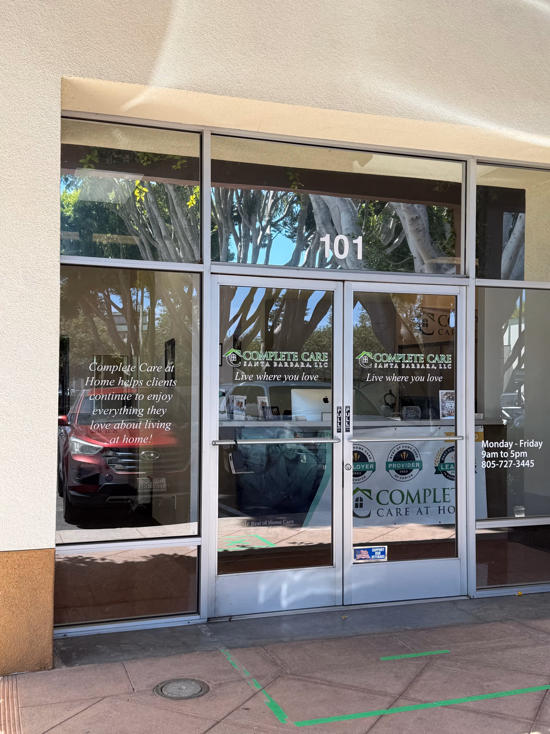 Glass entrance of Complete Care at Home with 101, reflecting trees.