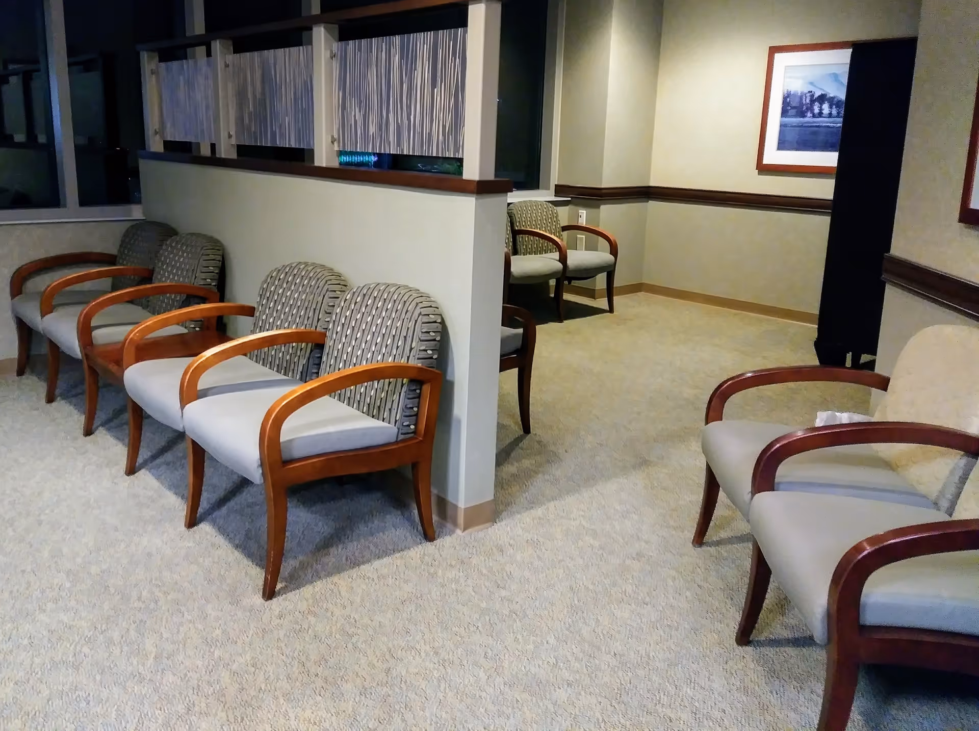 A waiting lounge with rows of cushioned chairs, a low partition, and framed art.