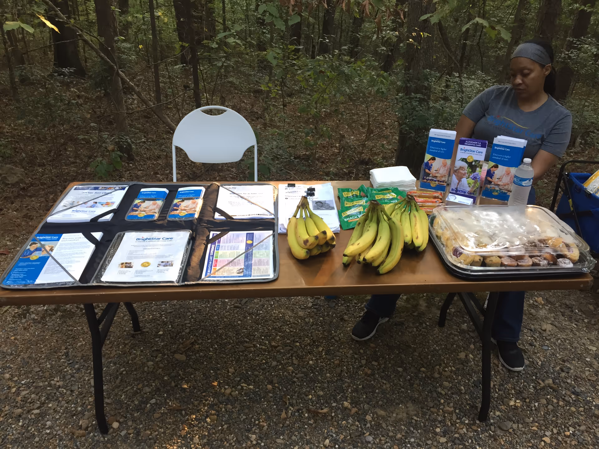 Outdoor information table with brochures, fruit, and a staff member at BrightStar Care.