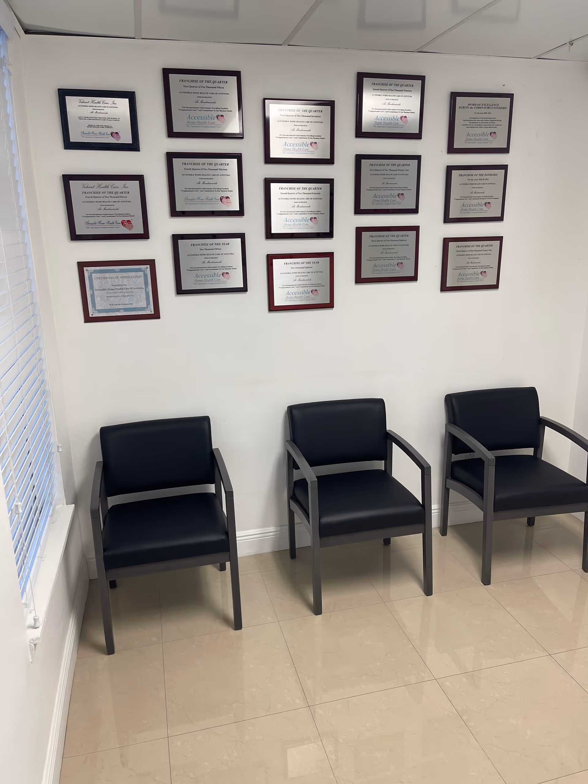 Waiting area with three black chairs and many framed certificates on the wall.