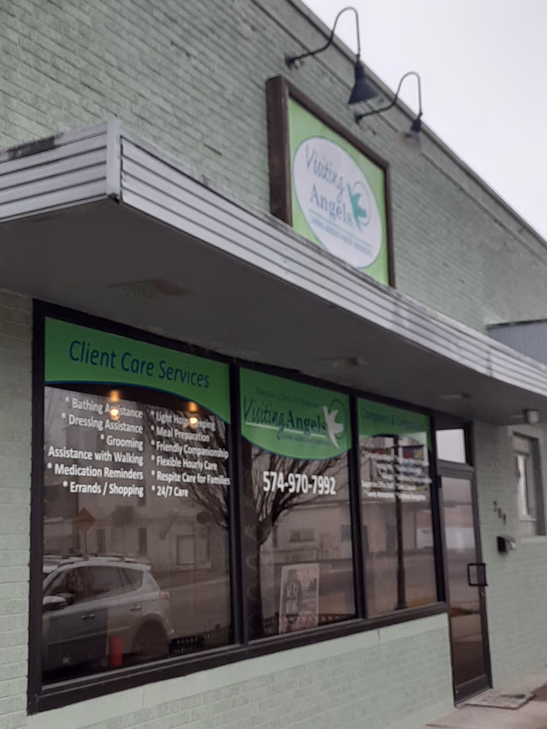 Front exterior of a green brick building with Visiting Angels sign and large windows.