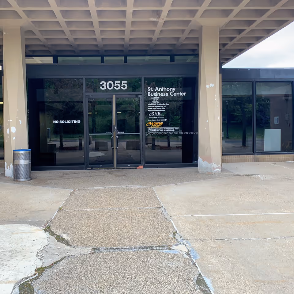 Front entrance of a commercial building with glass doors, signage, and a No Soliciting notice.