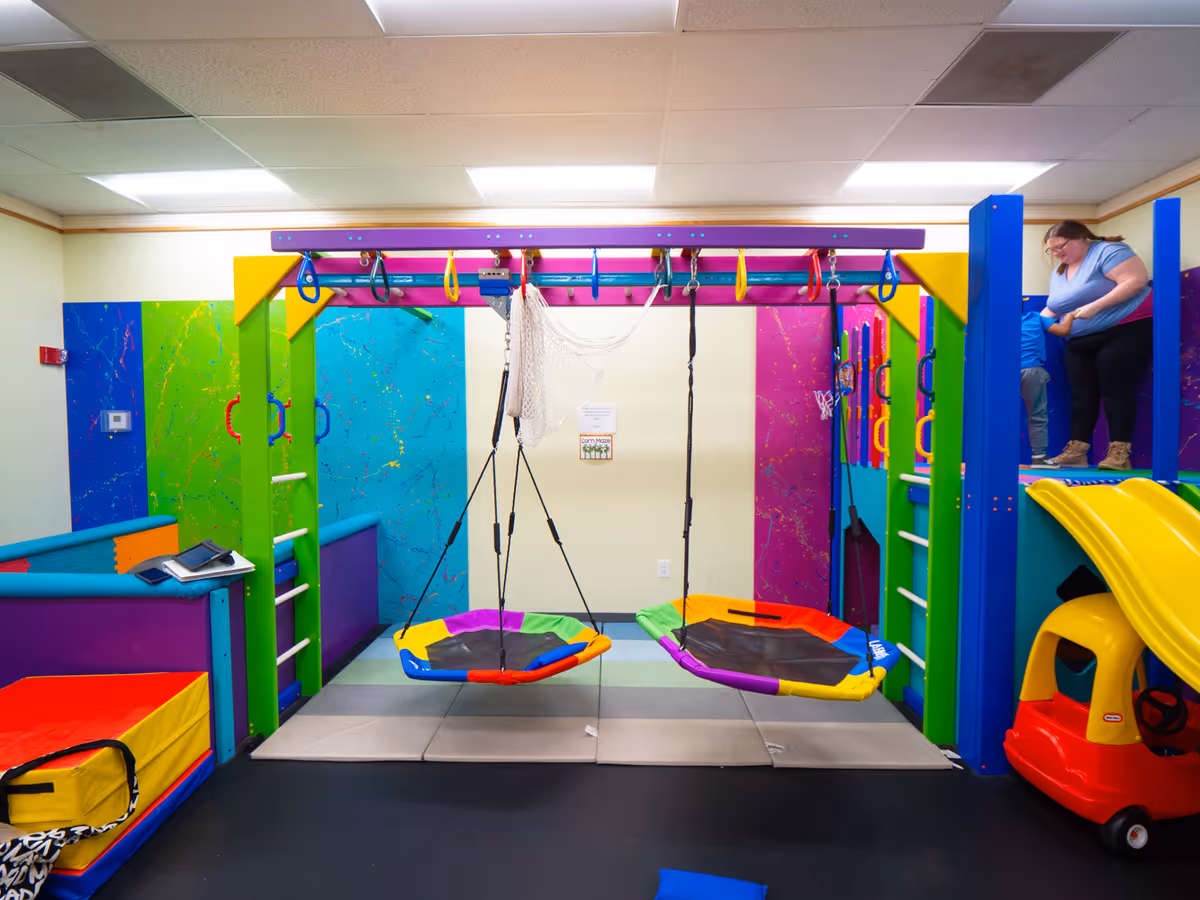 Indoor therapy play area with swings, a slide, and padded mats.
