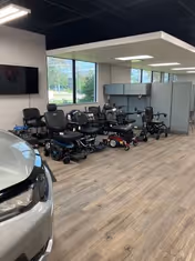 Showroom interior with multiple mobility scooters lined up beside a parked car.