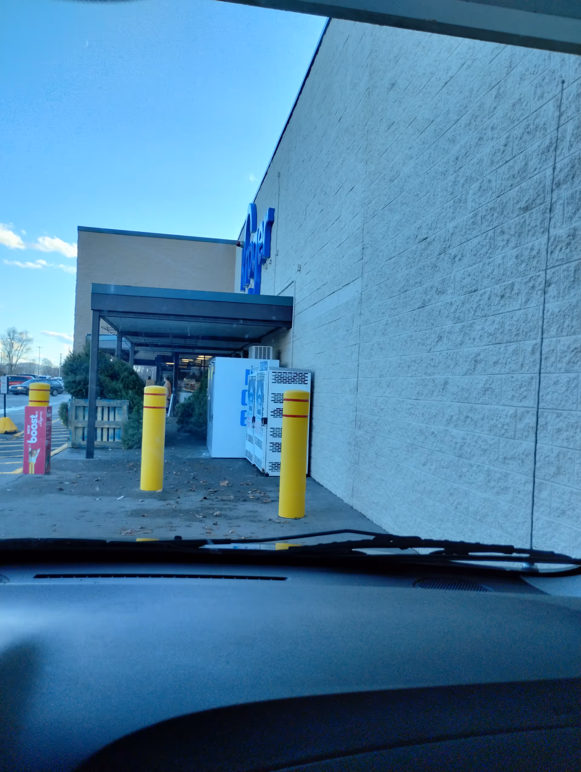 View from a car of Kroger Pharmacy entrance with blue sign and yellow bollards