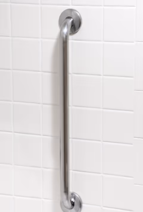 Stainless steel grab bar attached to white tiled bathroom wall.