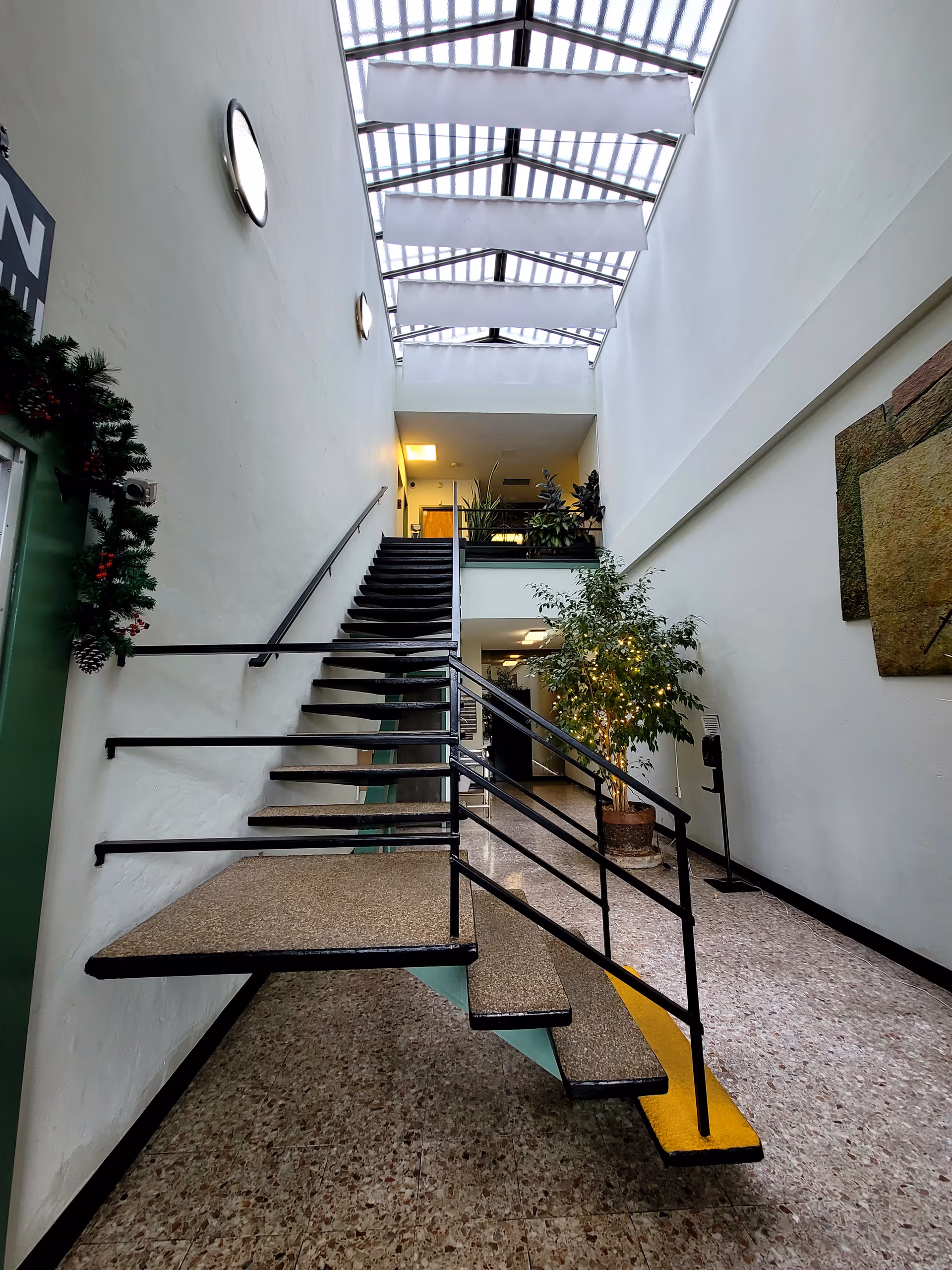 Bright interior atrium with a staircase, skylight roof, and potted plants.