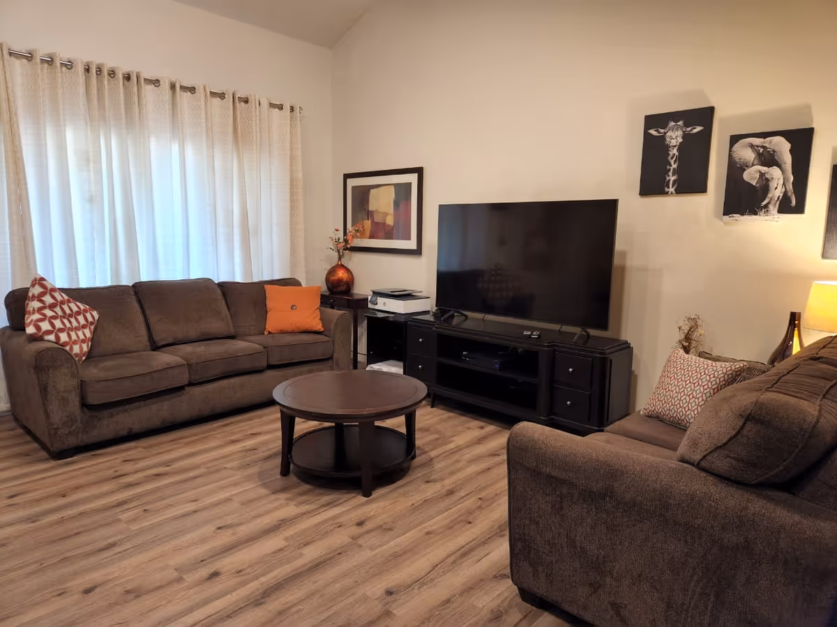Cozy living room with brown sofas, a round coffee table, and a large TV.