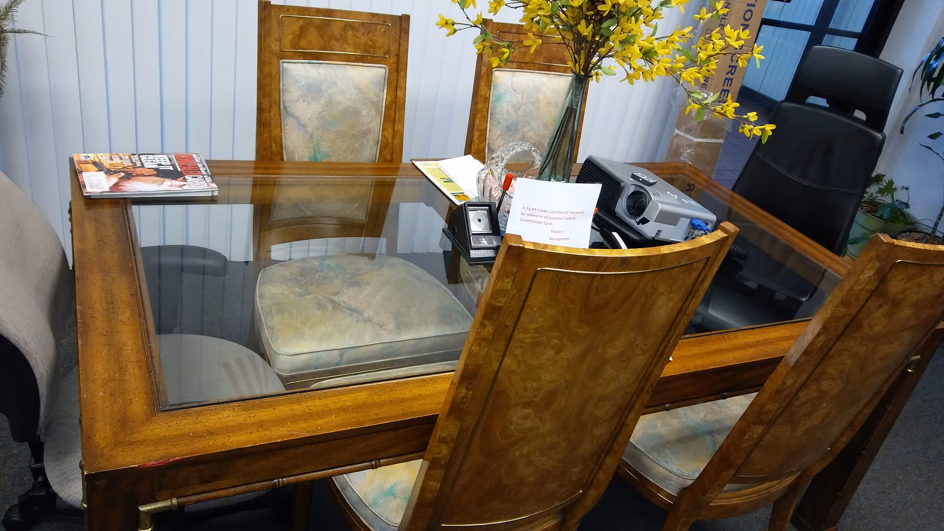 Wooden glass-top table with chairs and office items in an interior room.