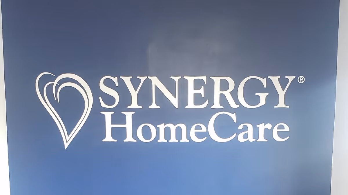 Blue wall with SYNERGY HomeCare logo and heart symbol.